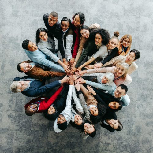 Draufsicht auf ein vielfältiges Team von Menschen, die in einem kooperativen und inklusiven Unternehmensumfeld die Hände reichen und damit Einheit und Teamarbeit symbolisieren.