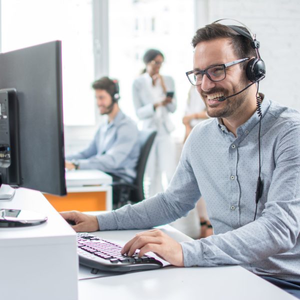 Lächelnde Kundendienstmitarbeiter mit Freisprech-Headset bei der Arbeit